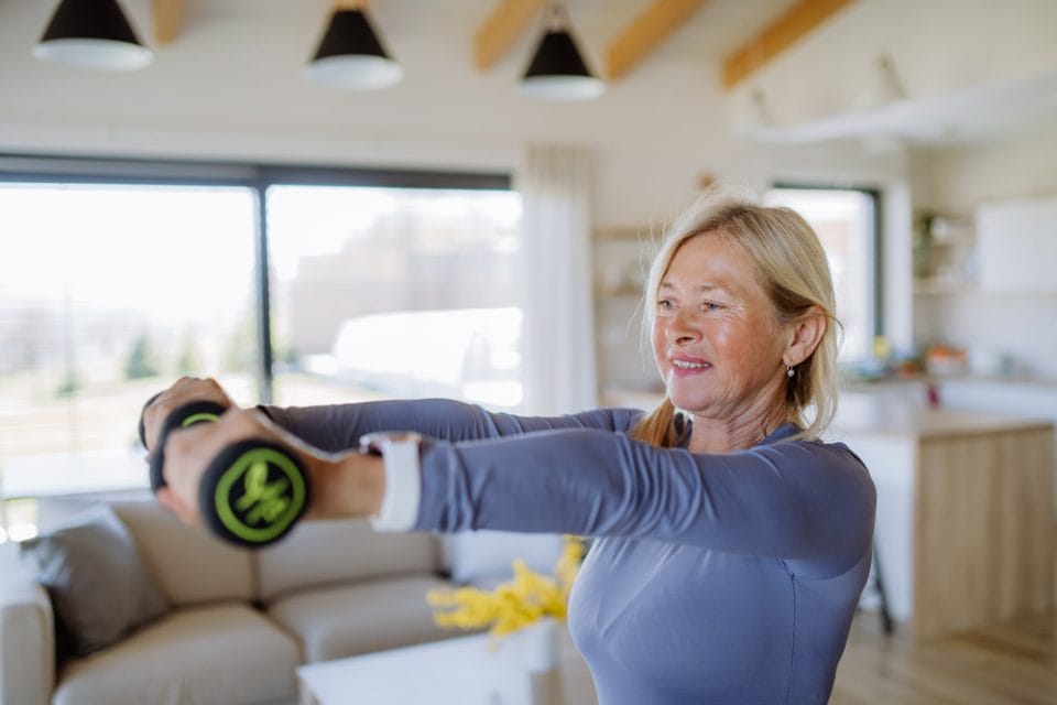 A fit senior woman exercising with dumbbells at home, active lifestyle concept.