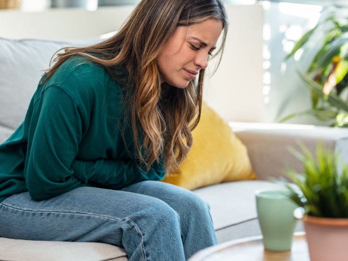 A young woman with a stomach ache leaning over on the couch.