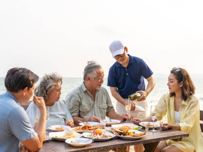 A happy family together on vacation with their senior parents, eating a quiet dinner at an outdoor restaurant.