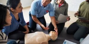 A CPR instructor guiding a group of students through the steps to accurately and properly perform CPR on an individual.