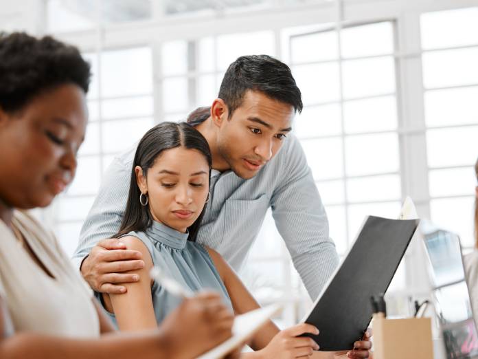 A group of employees sitting at the table with a male employee inappropriately touching a female employee.