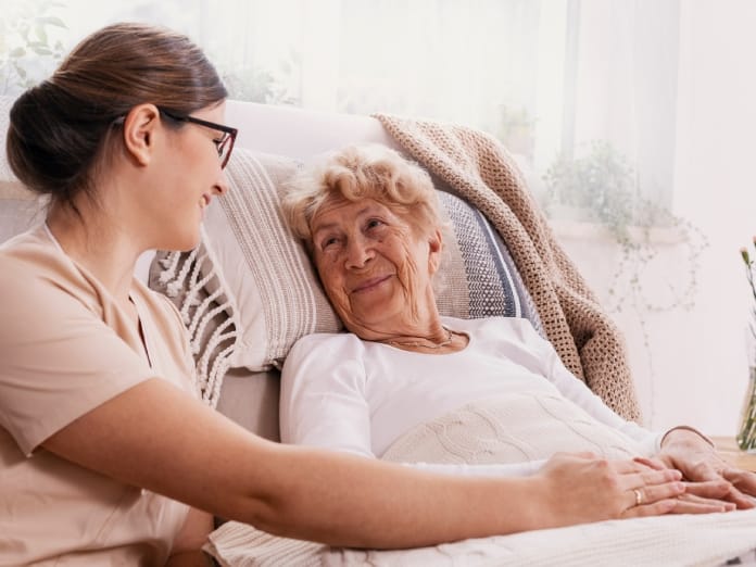 A senior woman sitting up in a hospital bed with an elevated head position. She smiles at a young woman holding her hand.