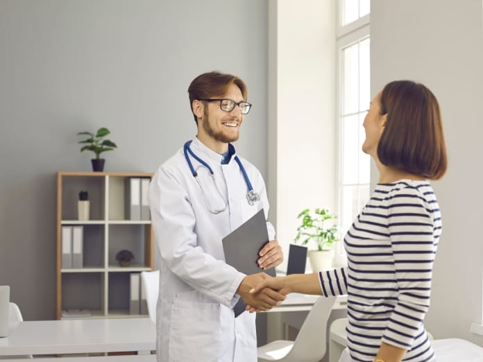 A doctor and his patient are having a positive interaction. They’re shaking hands and smiling at one another.