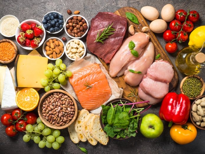 A table full of a variety of foods including lean meats, colorful vegetables, and crisp fruits. The platter is wooden.