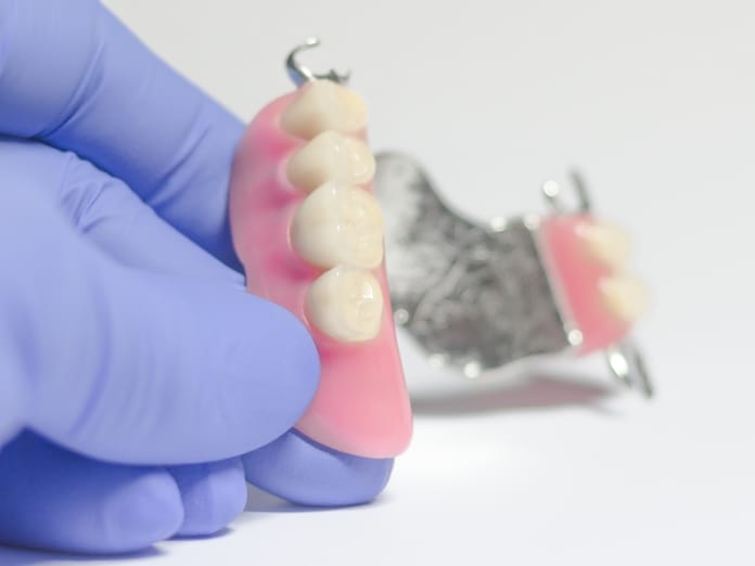 A close up of a dental provider in blue gloves. They're holding a set of partial dentures for someone's bottom teeth.