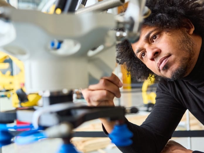 Close-up of a young engineer looking closely at manufacturing equipment, surrounded by other machinery.