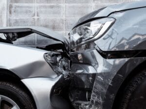 A close-up view shows a head on collision of a silver car and a gray SUV. A gray wall is in the background.