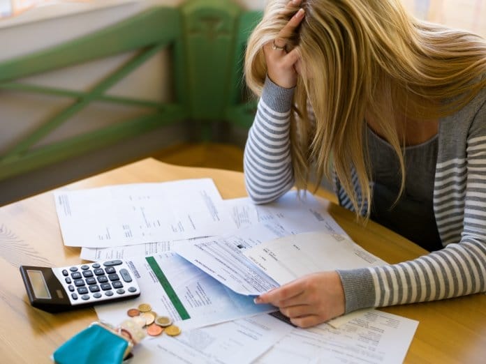 A woman sitting at her dining room table with her head in her hand as she stresses about finances. She has a calculator.