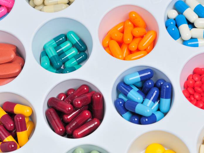 A close-up of an assortment of pills arranged on a tray. Each pill and capsule is a different color.