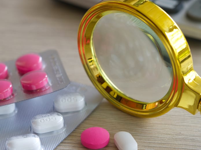 A close-up of white and pink pharmaceutical medication tablets next to a magnifying glass on a table.