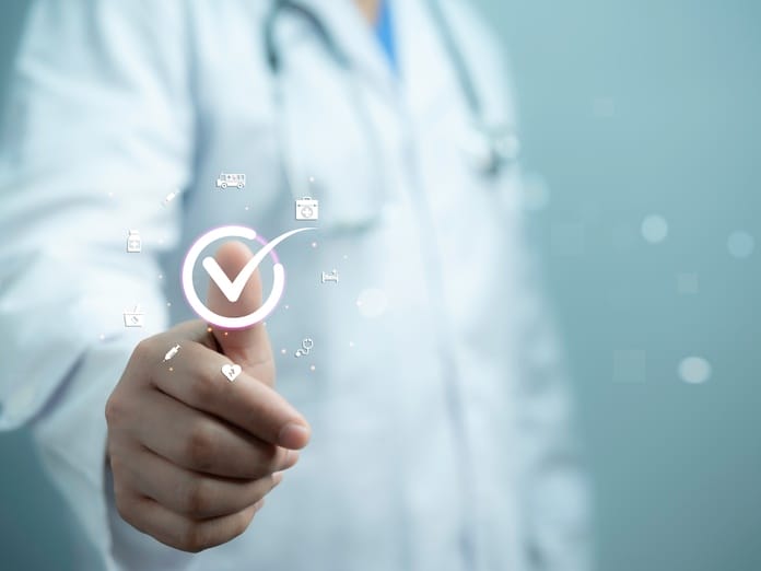 A doctor gives a thumbs-up behind a graphic featuring a white check mark in a circle with floating medical symbols.