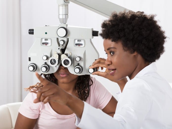 A patient sits behind a sight-testing machine as the ophthalmologist points to the screen.