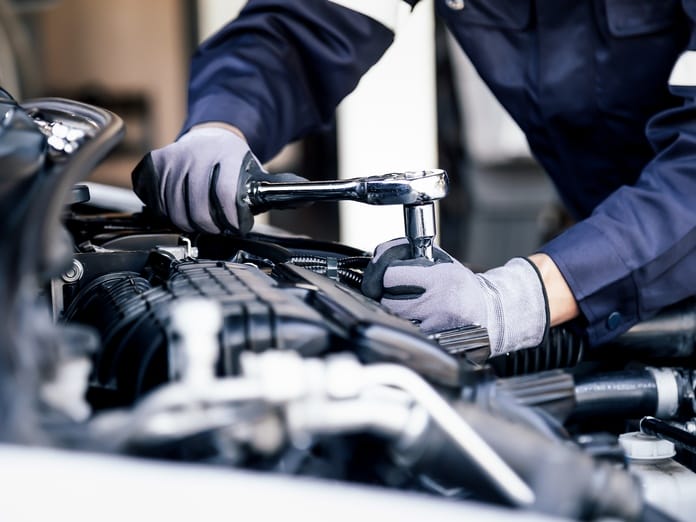 A close-up view of a mechanic's gloved hands as they use a wrench to tighten a piece in the engine compartment.