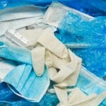 Used masks, gloves, and gowns fill a red medical waste bin, showing the disposal of medical protective gear.