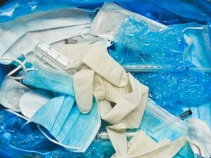 Used masks, gloves, and gowns fill a red medical waste bin, showing the disposal of medical protective gear.