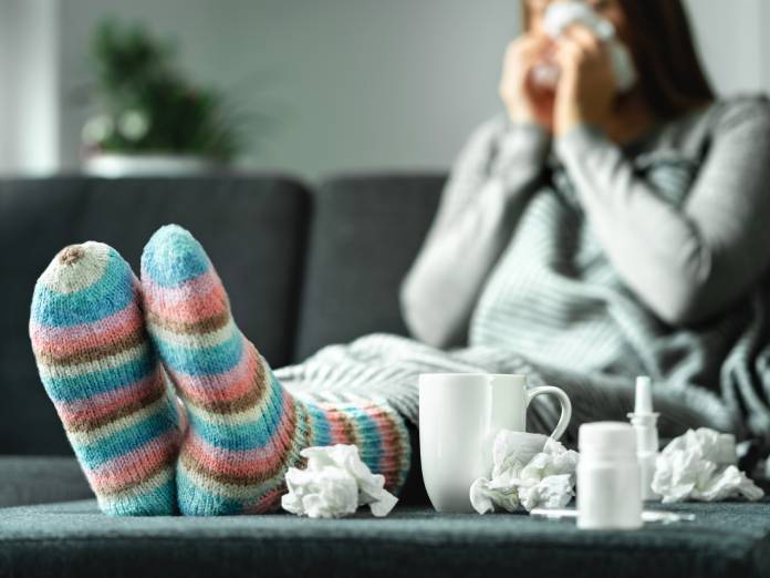 A sick person at home on the couch with their feet propped on the coffee table. There are tissues on the table.