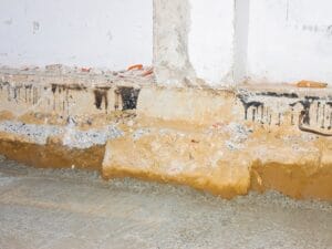 Yellow-colored insulation from water damage shown against the cement wall of a crawl space in a basement.