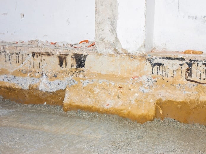 Yellow-colored insulation from water damage shown against the cement wall of a crawl space in a basement.