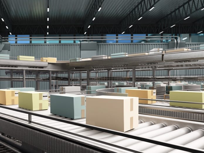 A large warehouse contains a conveyor belt with blue, yellow, orange, and brown cardboard boxes on it.