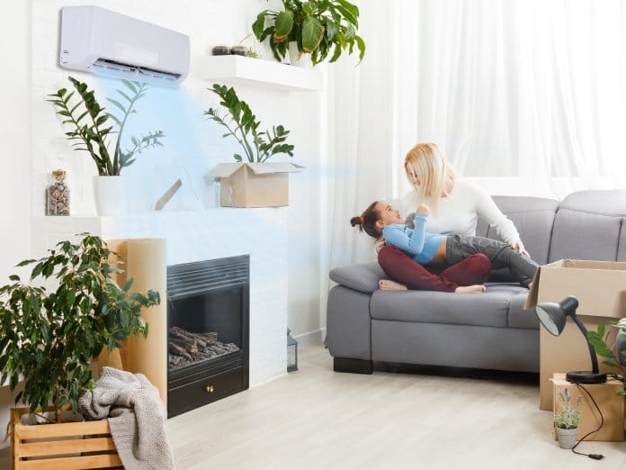 A woman and young girl playing on a couch, surrounded by indoor plants and cardboard boxes on the floor.