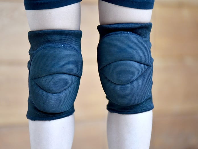A close-up view of a person's thick black kneepads. The used protective gear is tight on the wearer's legs.