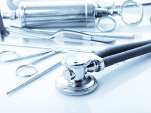 A close-up of medical equipment scattered on a white surface. The equipemnt includes ENT tools and a stethoscope.