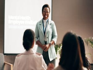 A happy Black health professionalwoman smiles as she speaks to a room of aspiring health professionals.